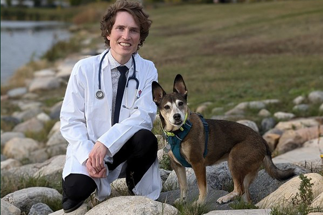 Veterinary student Chris Keane with his dog Ravenclaw alongside a small pond. 