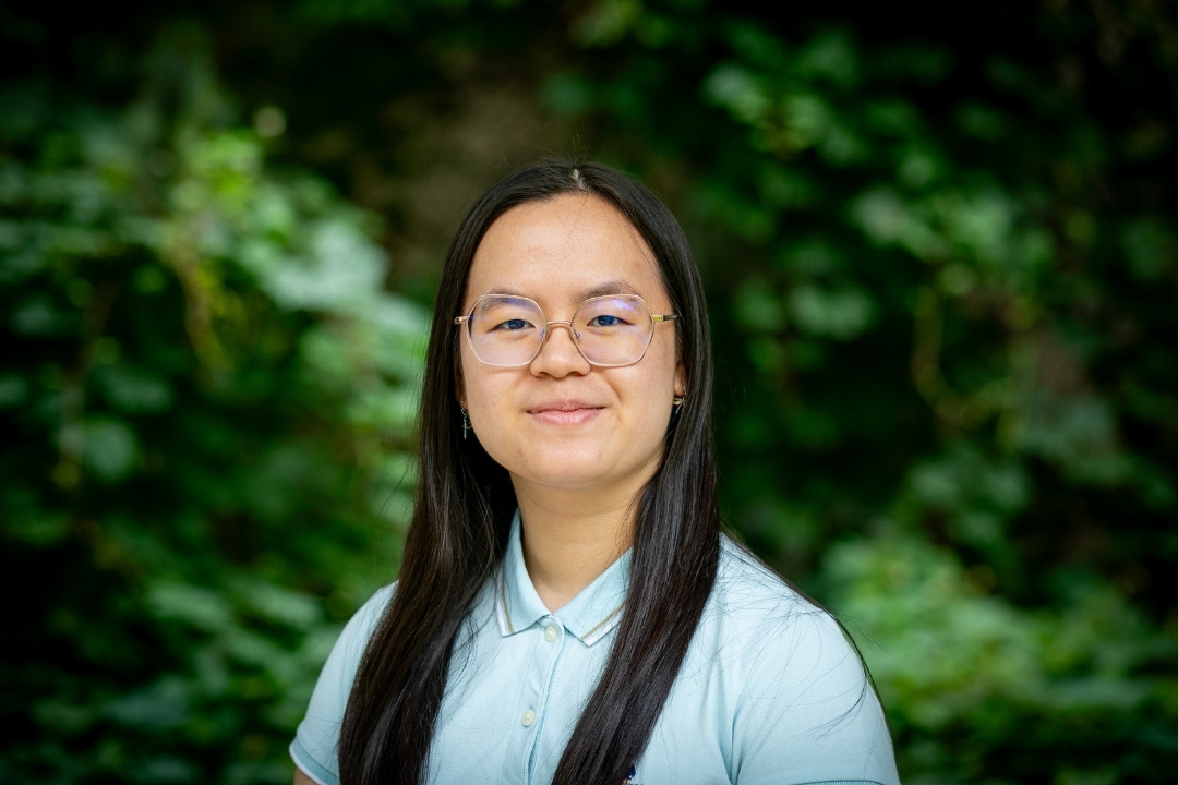 Minh Thanh (Agnes) Truc Nguyen in a blue shirt with a green, leafy background.