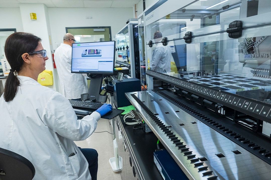 Woman in safety glass and a lab coat looking at a computer screen.