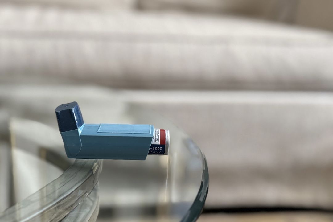 A blue rescue inhaler sits on top of a glass table.